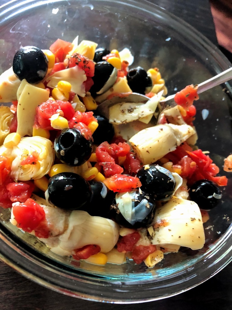 A picture of a salad with olives, artichokes, tomatoes, and corn.
